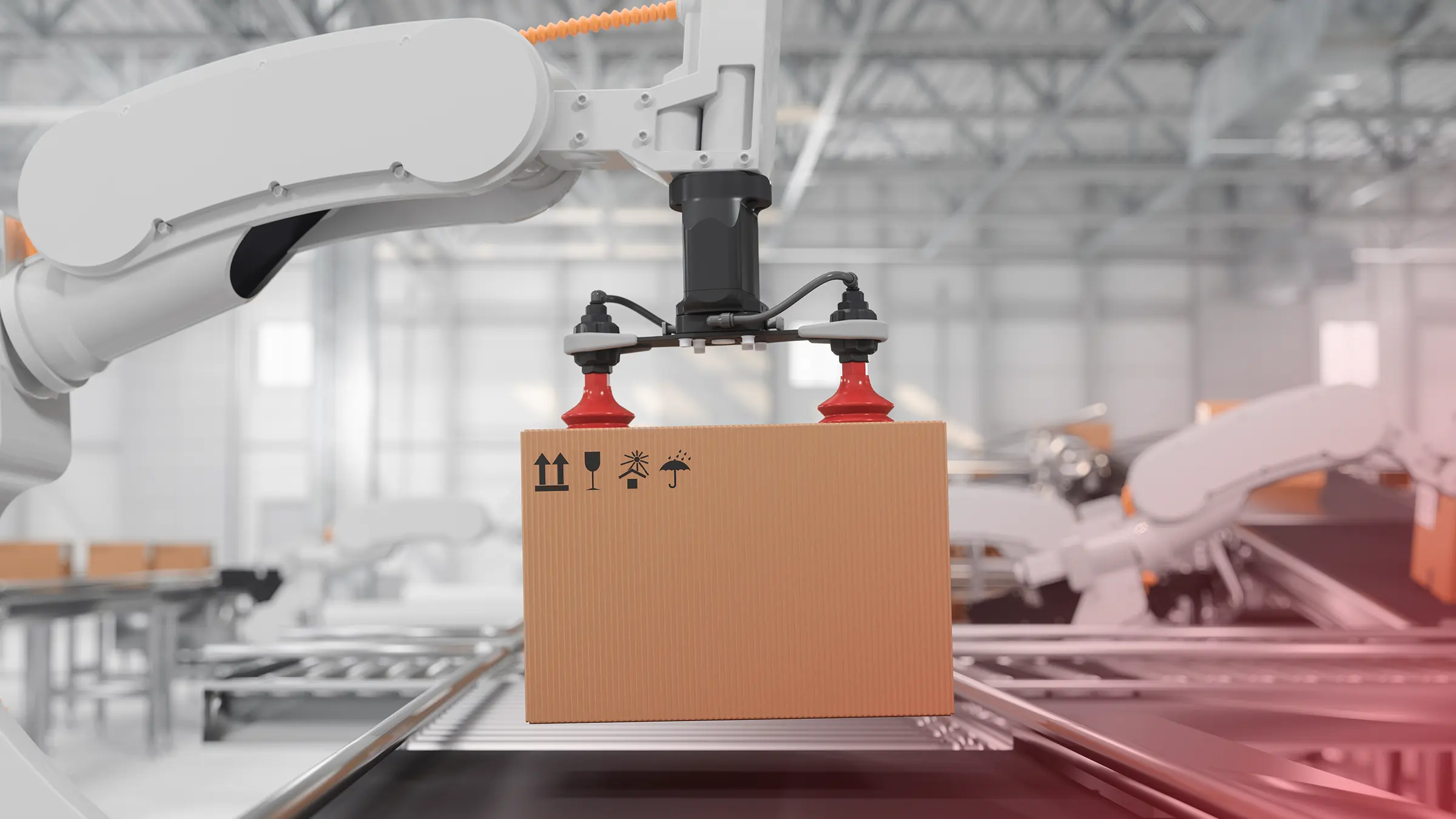 A white robotic arm with red suction cups lifts a cardboard box