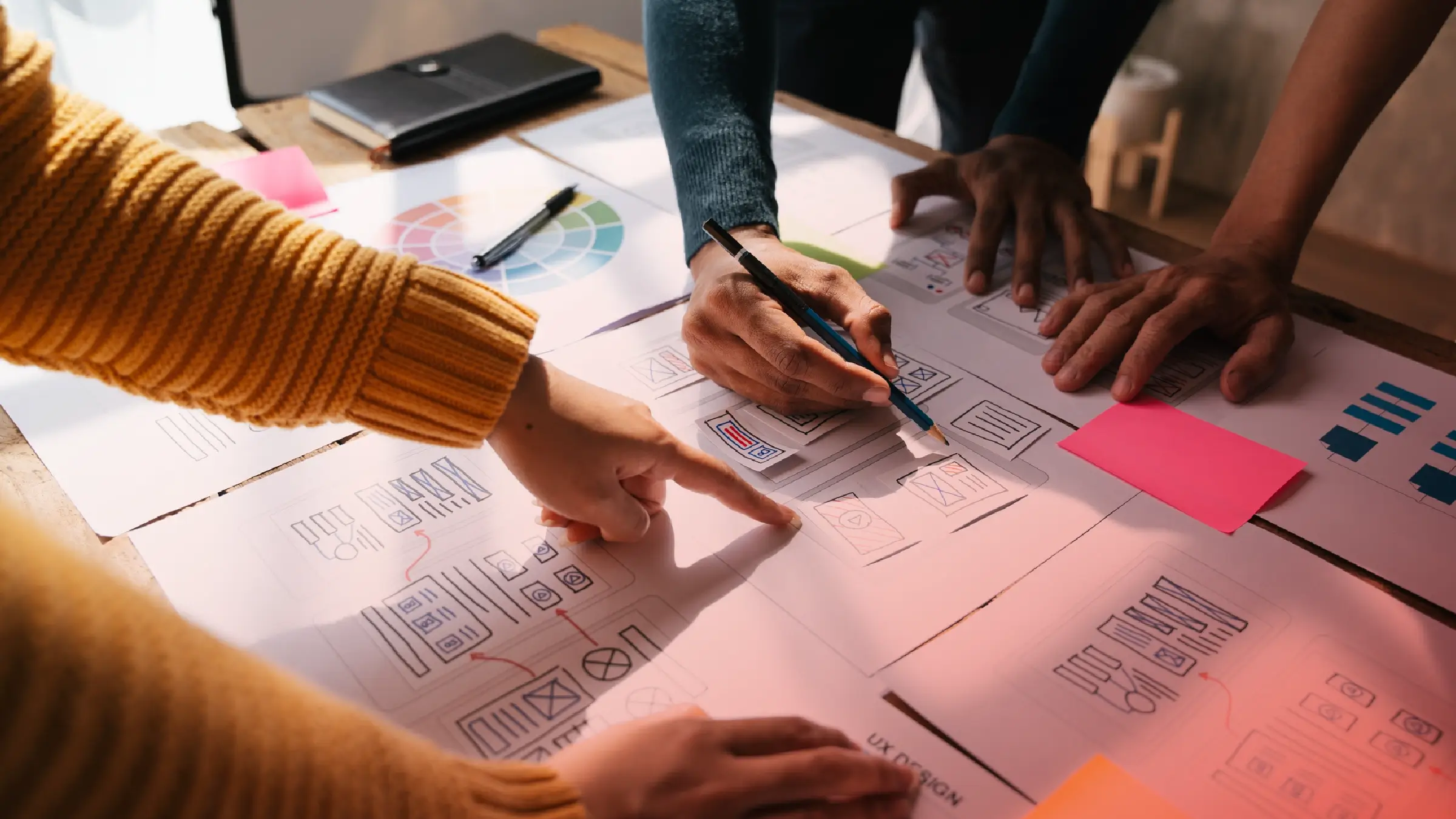 Team collaborating on UX design wireframes, reviewing layout sketches and user flow diagrams on a table covered with papers.